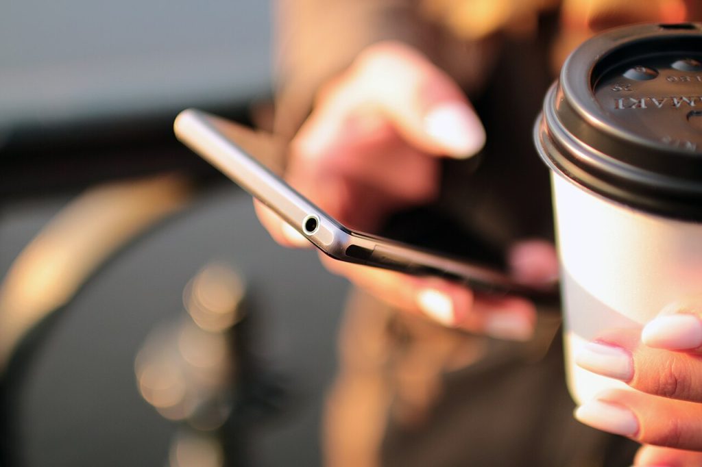 Hænder med smartphone og kaffe